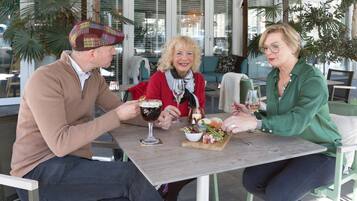 Trois personnes sont assises à une table à l’extérieur, devant un repas et des boissons.