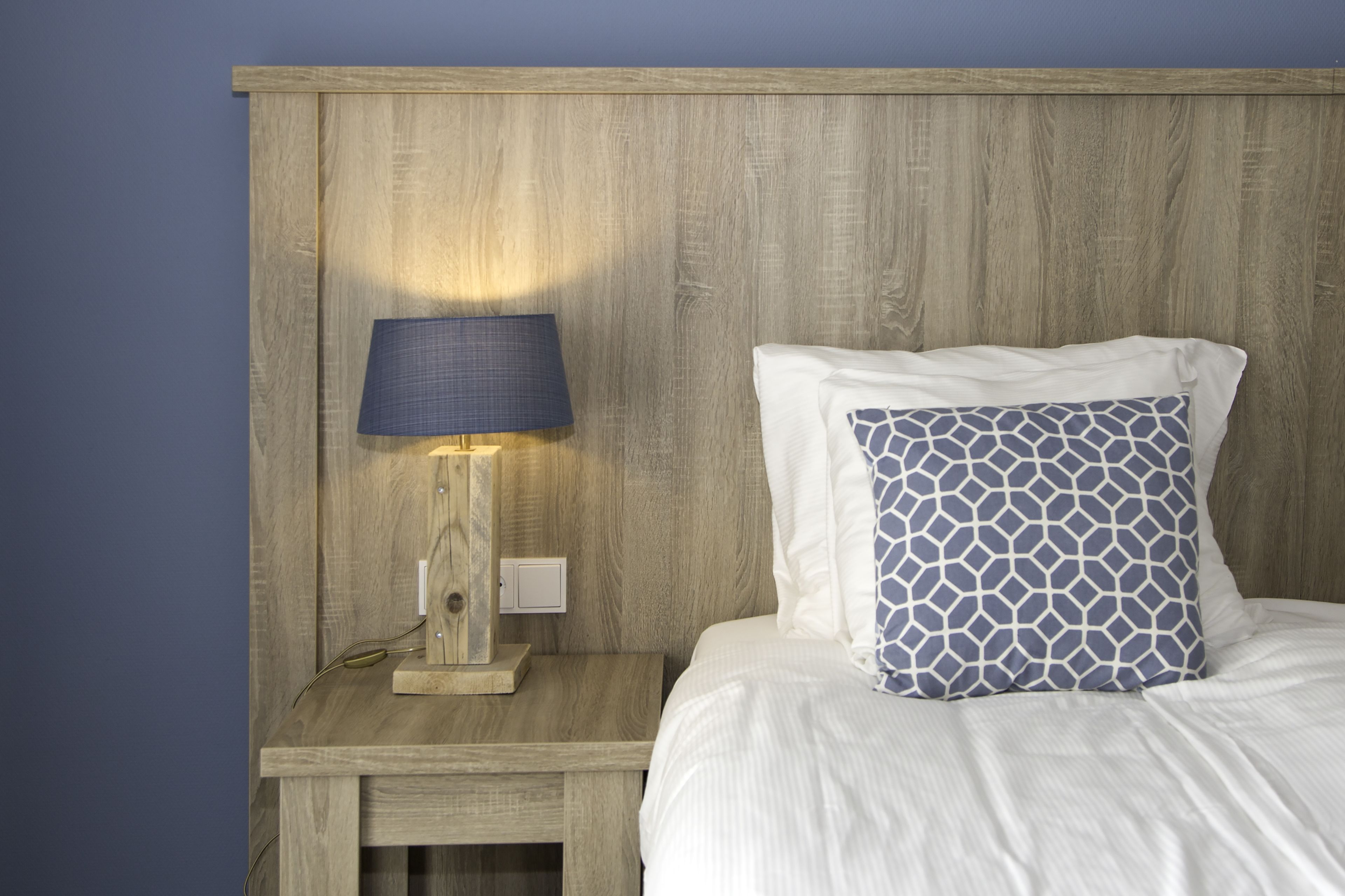 A neatly made bed with a patterned pillow and a bedside lamp on a wooden nightstand.