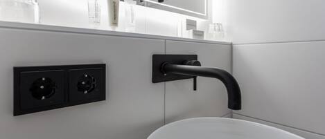 A bathroom with a white sink, black faucet, and two electrical outlets on the wall.