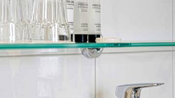 A bathroom with a glass shelf holding toiletries and a chrome faucet.