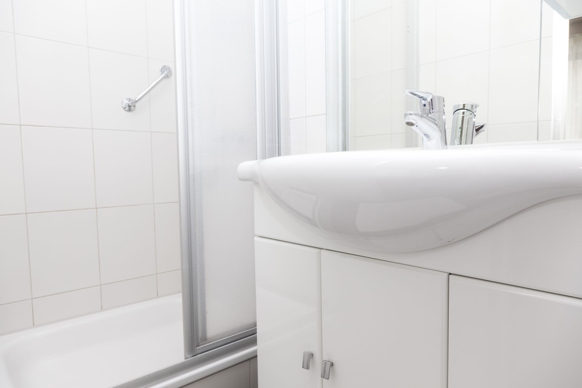 Ein modernes Badezimmer mit einem weißen Waschbecken, einer Dusche und einem Glasduschaumraum.