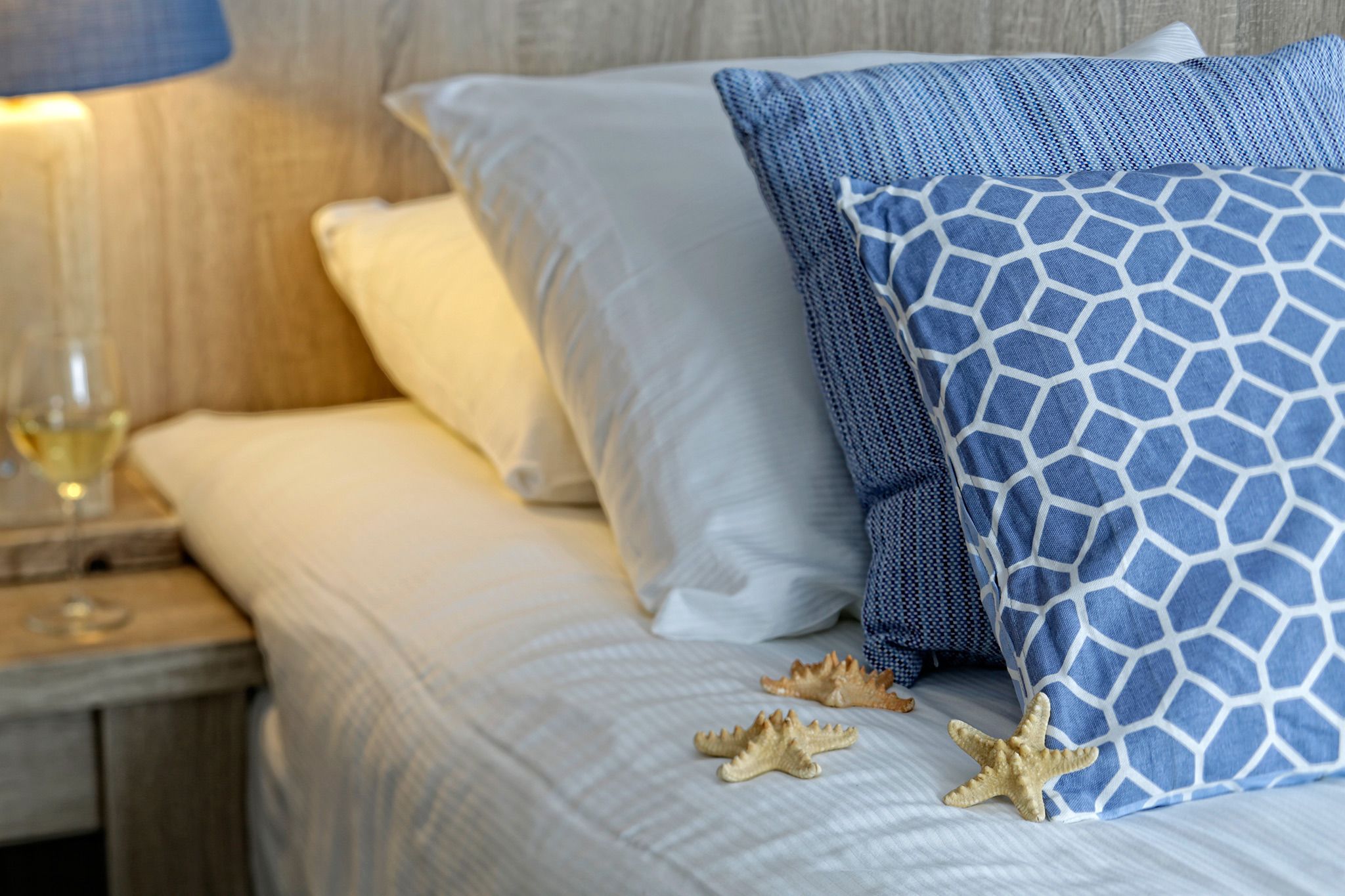 A bed with white and blue patterned pillows, a wooden nightstand with a glass, and starfish decorations.