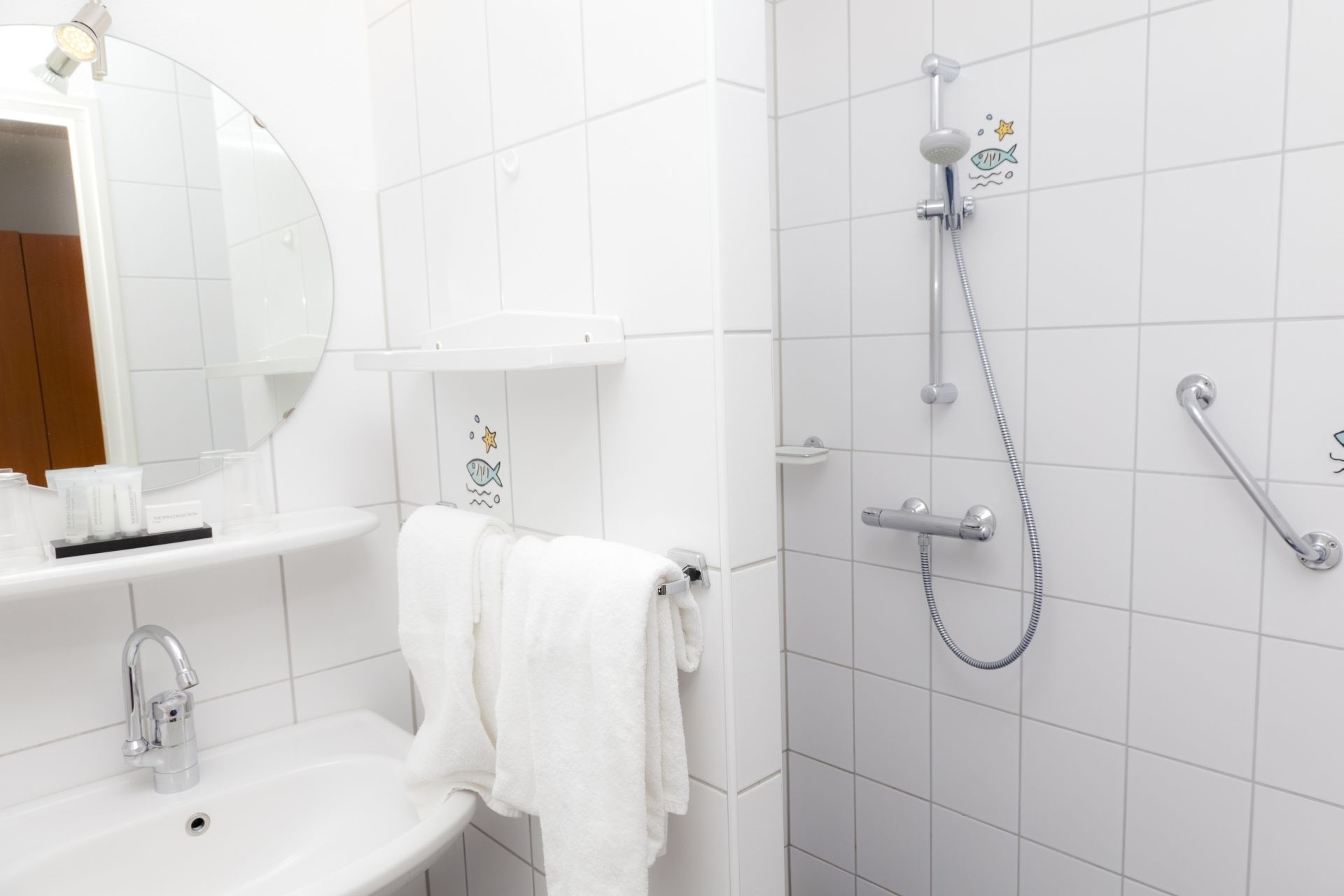 Un baño con lavamanos, espejo, toallero y ducha con cabezal de ducha de mano y grifo empotrado.