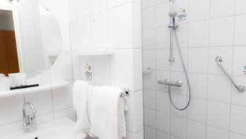 Un baño con lavamanos, espejo, toallero y ducha con cabezal de ducha de mano y grifo empotrado.