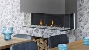 Un interior moderno con chimenea, papel tapiz estampado y una zona de comedor con sillas y mesa.