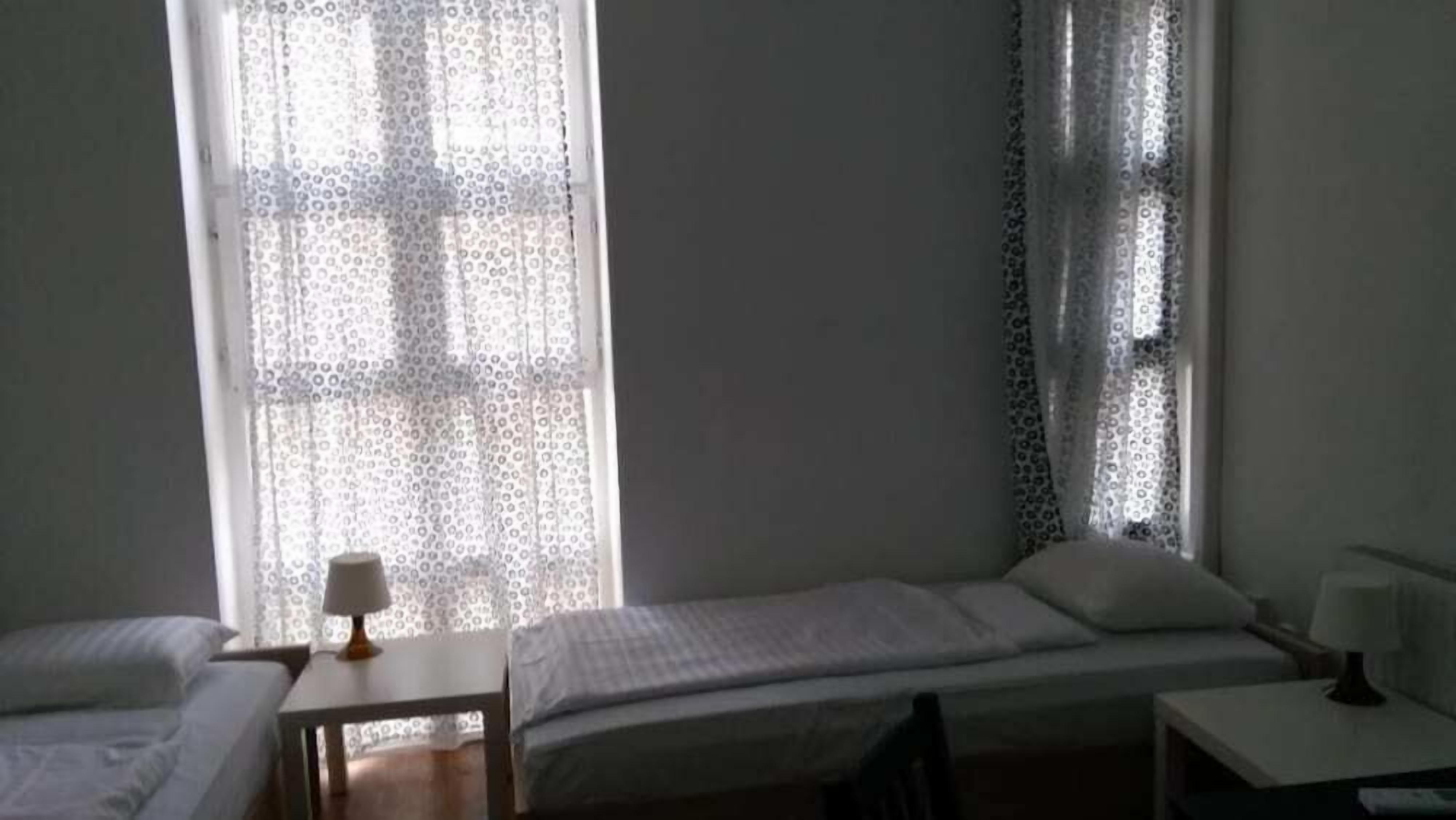 A room with two single beds, a small table, and a window with patterned curtains.