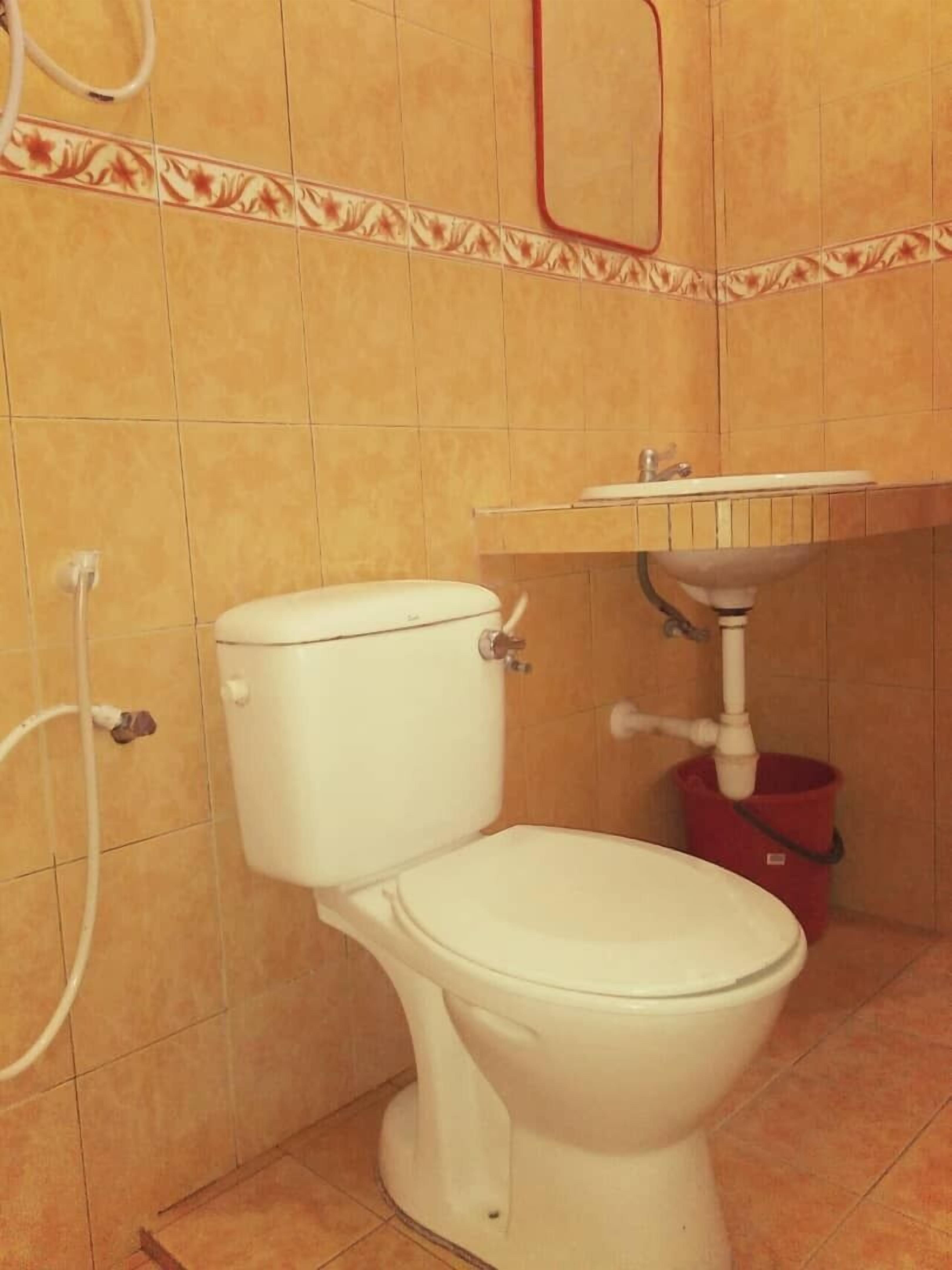 A bathroom with a toilet, a sink, and a red bucket.