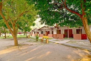A row of traditional-style buildings with a sandy ground, benches, and trees providing shade. - Vikri Beach Resort (Pangkor Island)