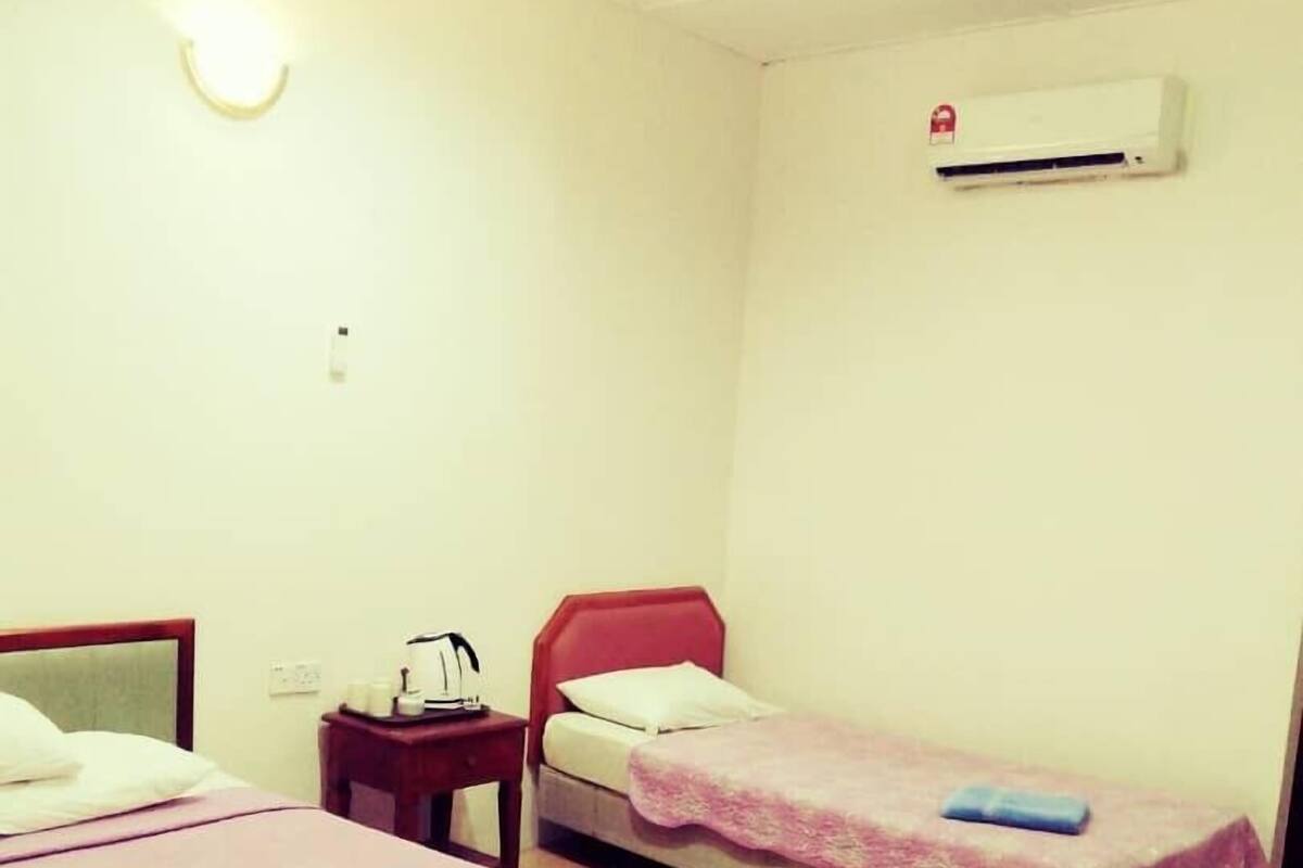 Een kamer met twee éénpersoonsbedden, een nachtkastje met een lamp, een rode stoel en een airconditioning aan de muur.