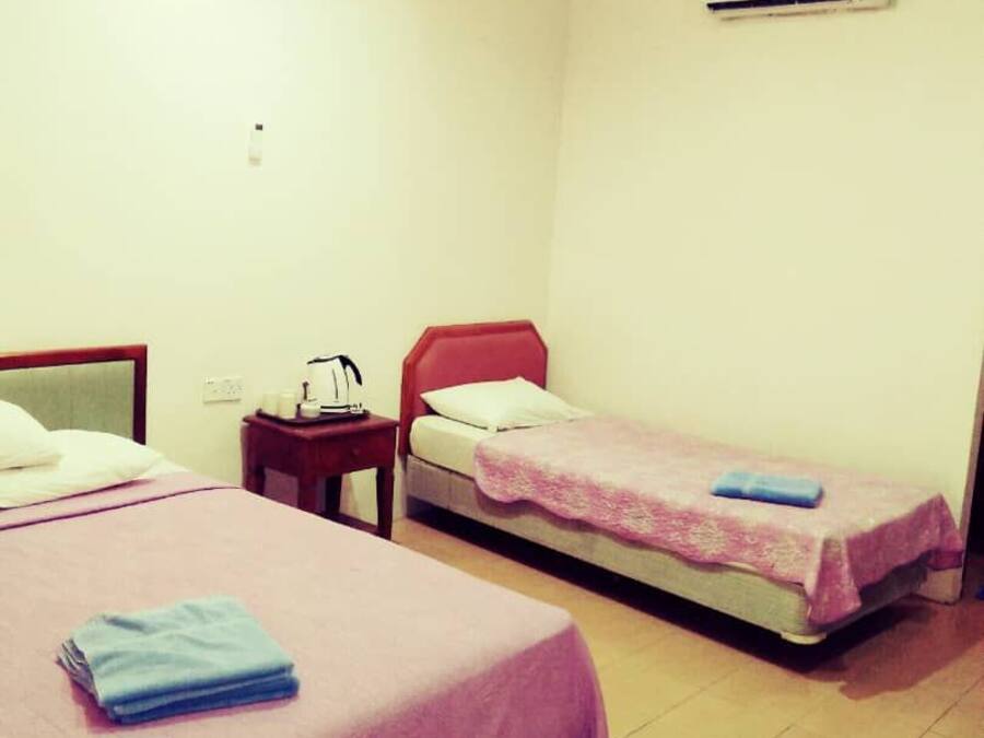 A hotel room with two beds, a nightstand, a chair, an air conditioning unit, and a wall socket.