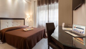 Una camera d'albergo con un letto, una scrivania con un portatile, una sedia e una finestra con tende.
