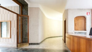 Un'hall dell'hotel con una reception, una porta in legno e una vetrata che dà su un'altra stanza.