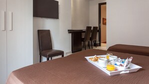 Una camera d'albergo con un letto, un vassoio per la colazione con croissant, caffè e succo d'arancia, e una TV montata a parete.