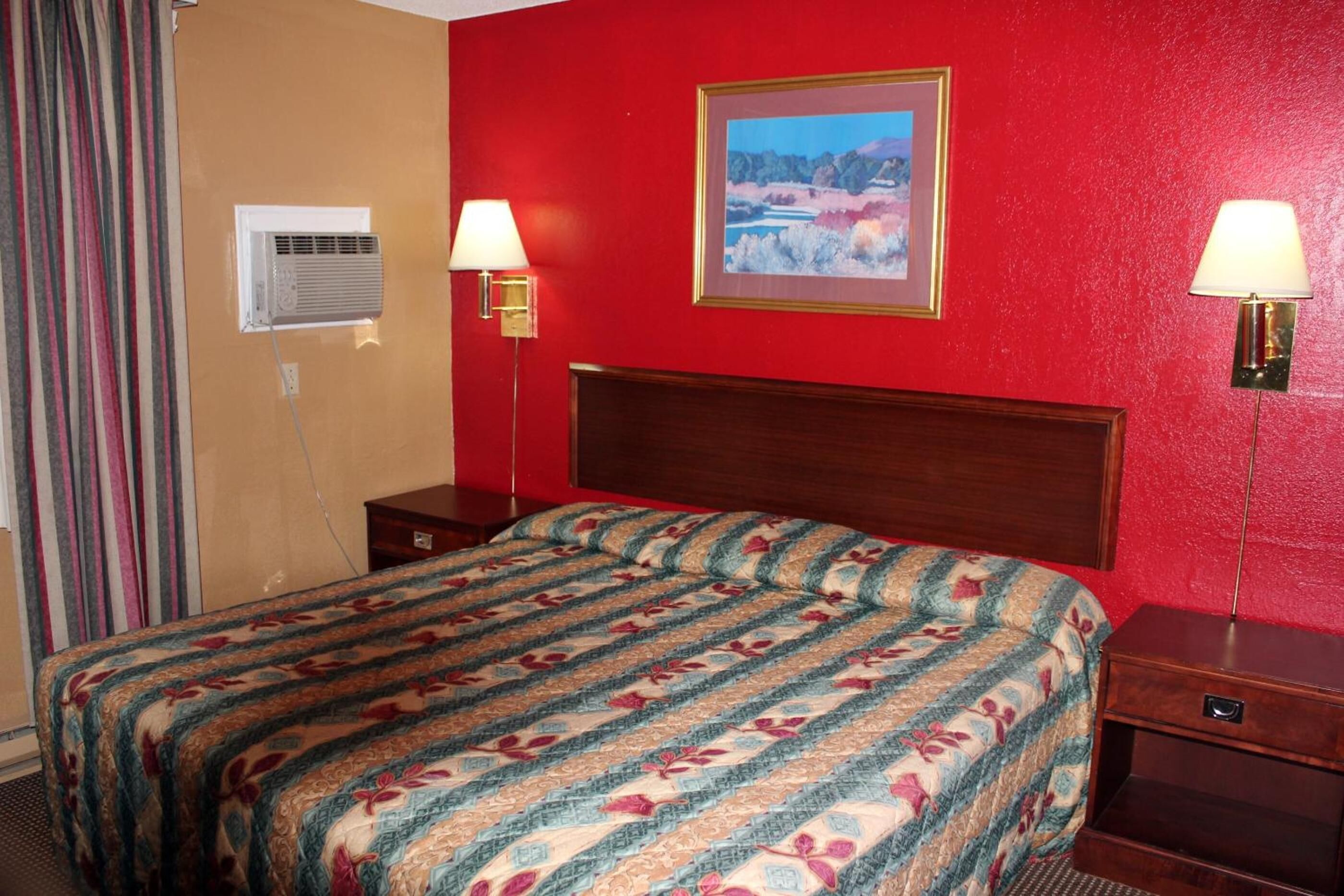 A hotel room with a large bed, two bedside lamps, a framed picture on the wall, and an air conditioning unit.