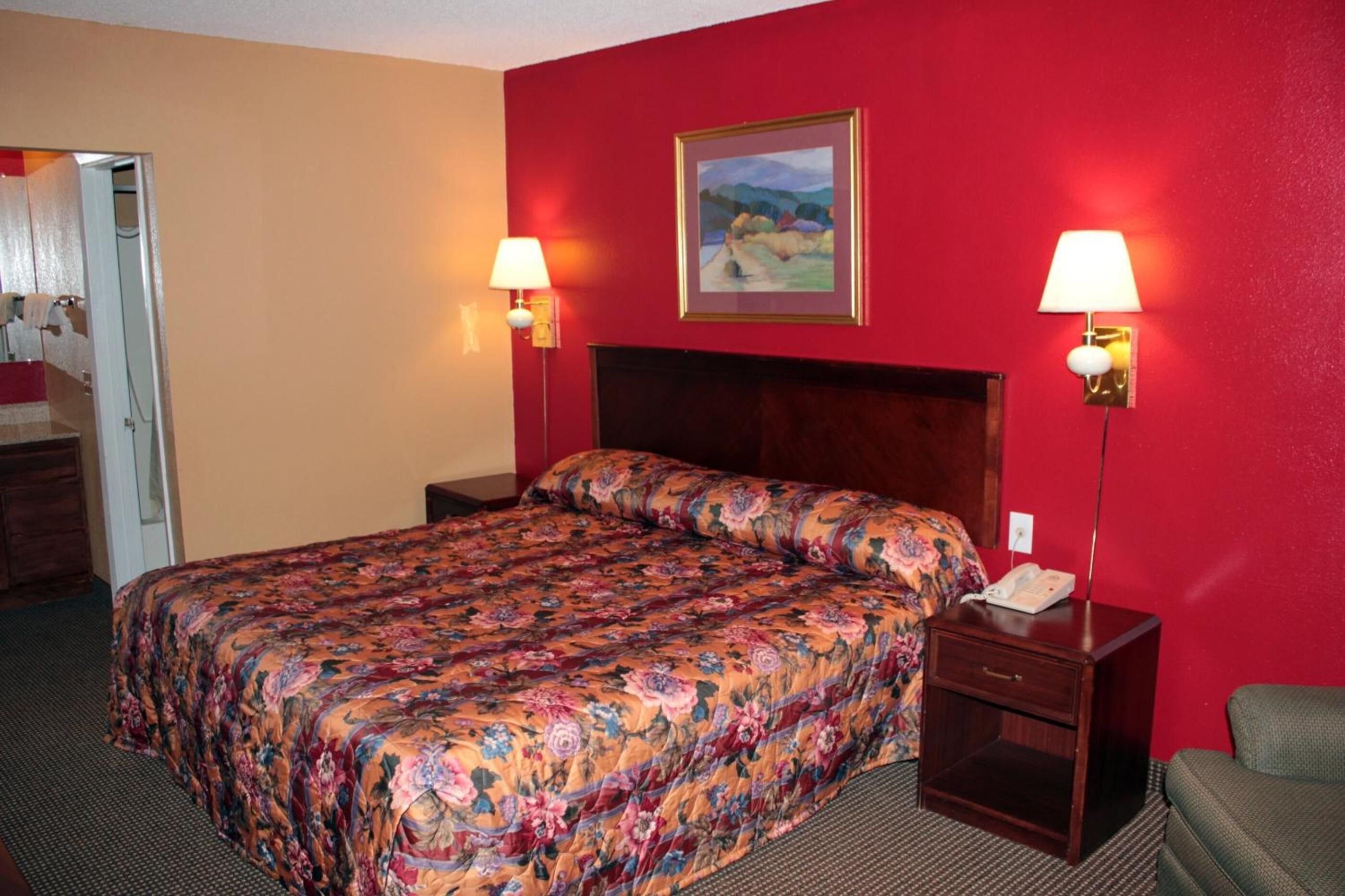 A hotel room with a floral bedspread, a wooden headboard, two bedside lamps, a painting on the wall, and a telephone on the nightstand.