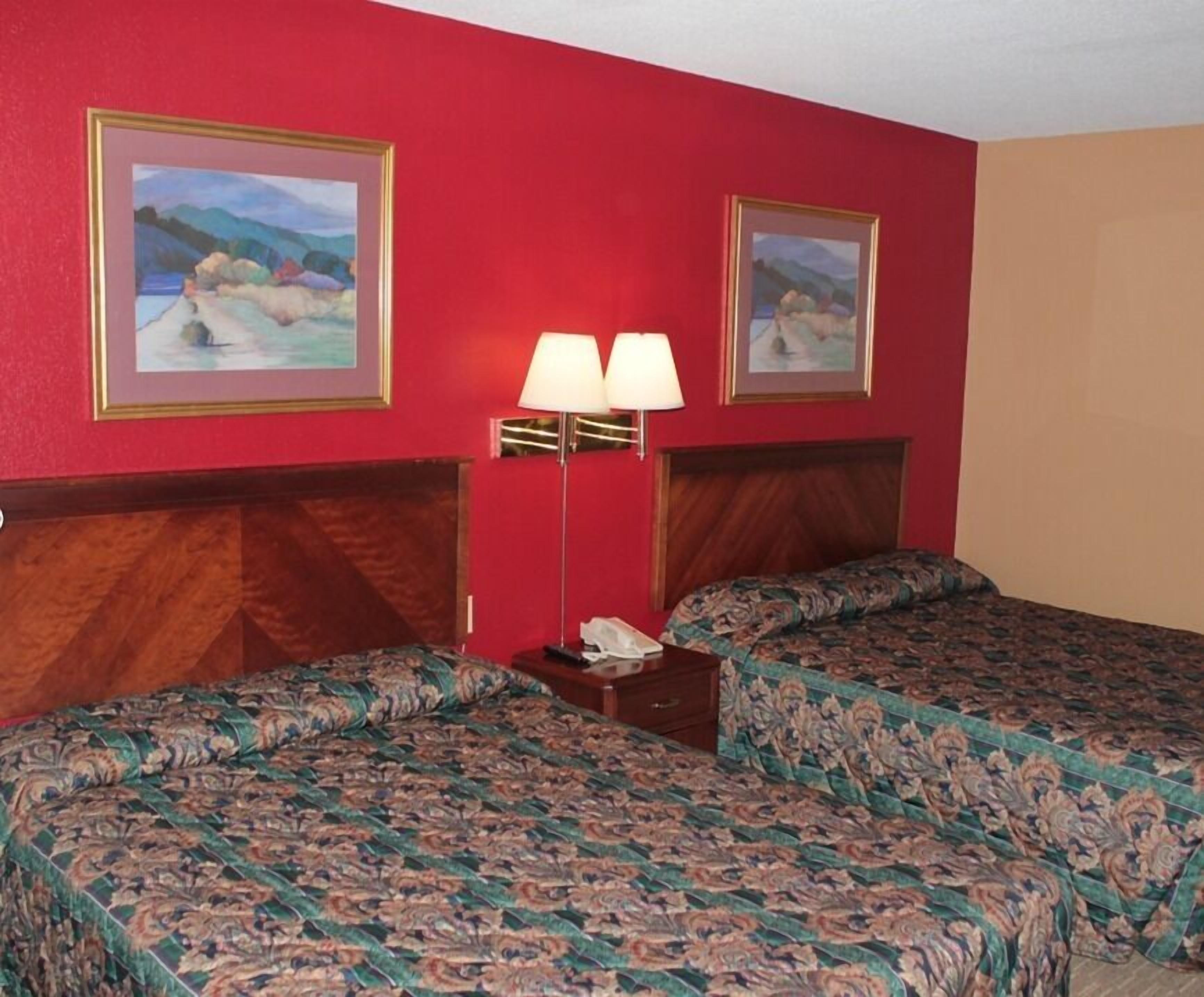 A hotel room with two beds, a nightstand, and two wall-mounted lamps.