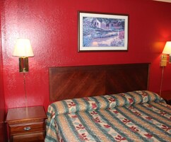 Una habitación de hotel con cabecera de madera, cama con colcha estampada de flores, mesita de noche con lámpara y un cuadro enmarcado en la pared.