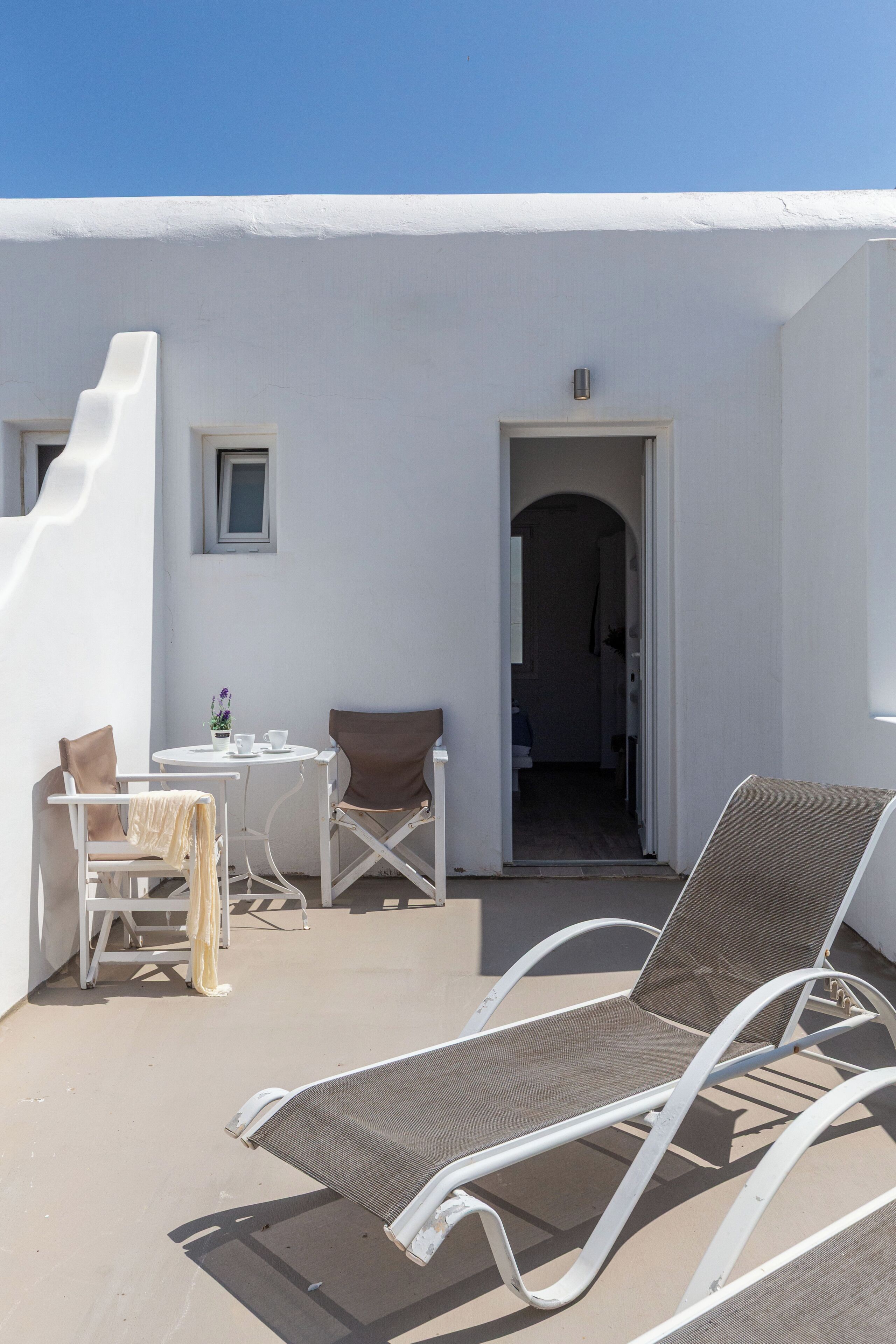 A white building with a balcony, a table with chairs, and a door leading to an interior space.