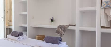 Une chambre à coucher comprenant un lit, un téléviseur à écran plat fixé au mur et une armoire avec des vêtements suspendus.