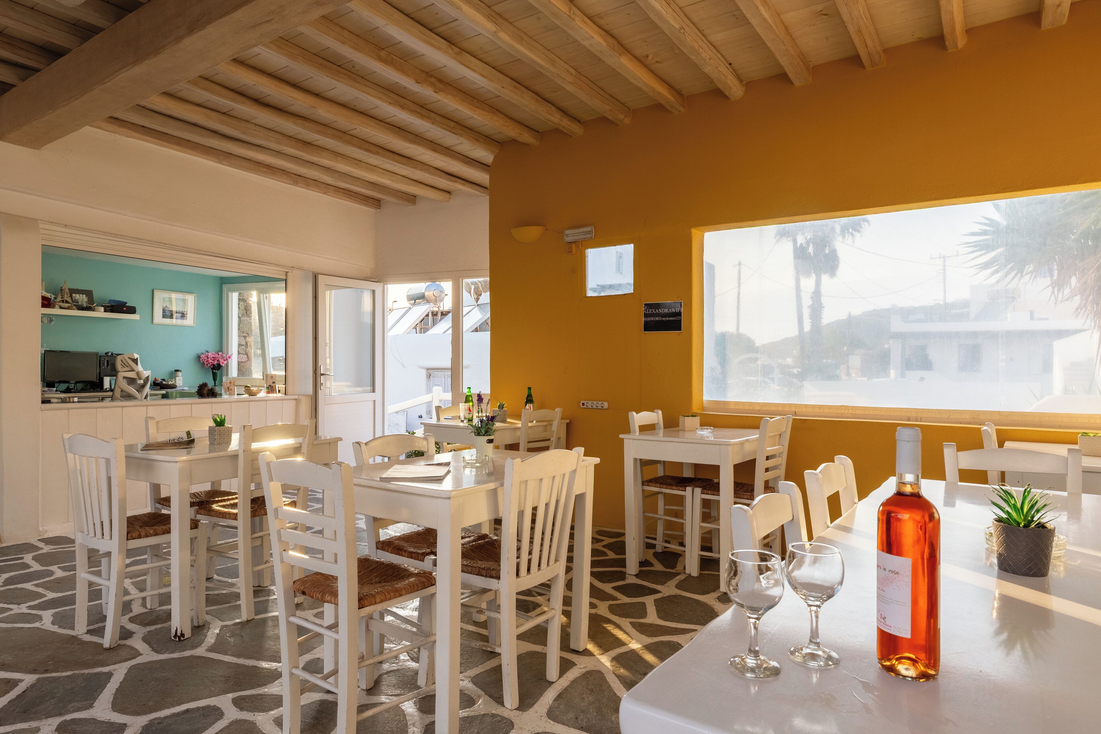 Un restaurante con mobiliario blanco, un ventanal grande y suelo de piedra.