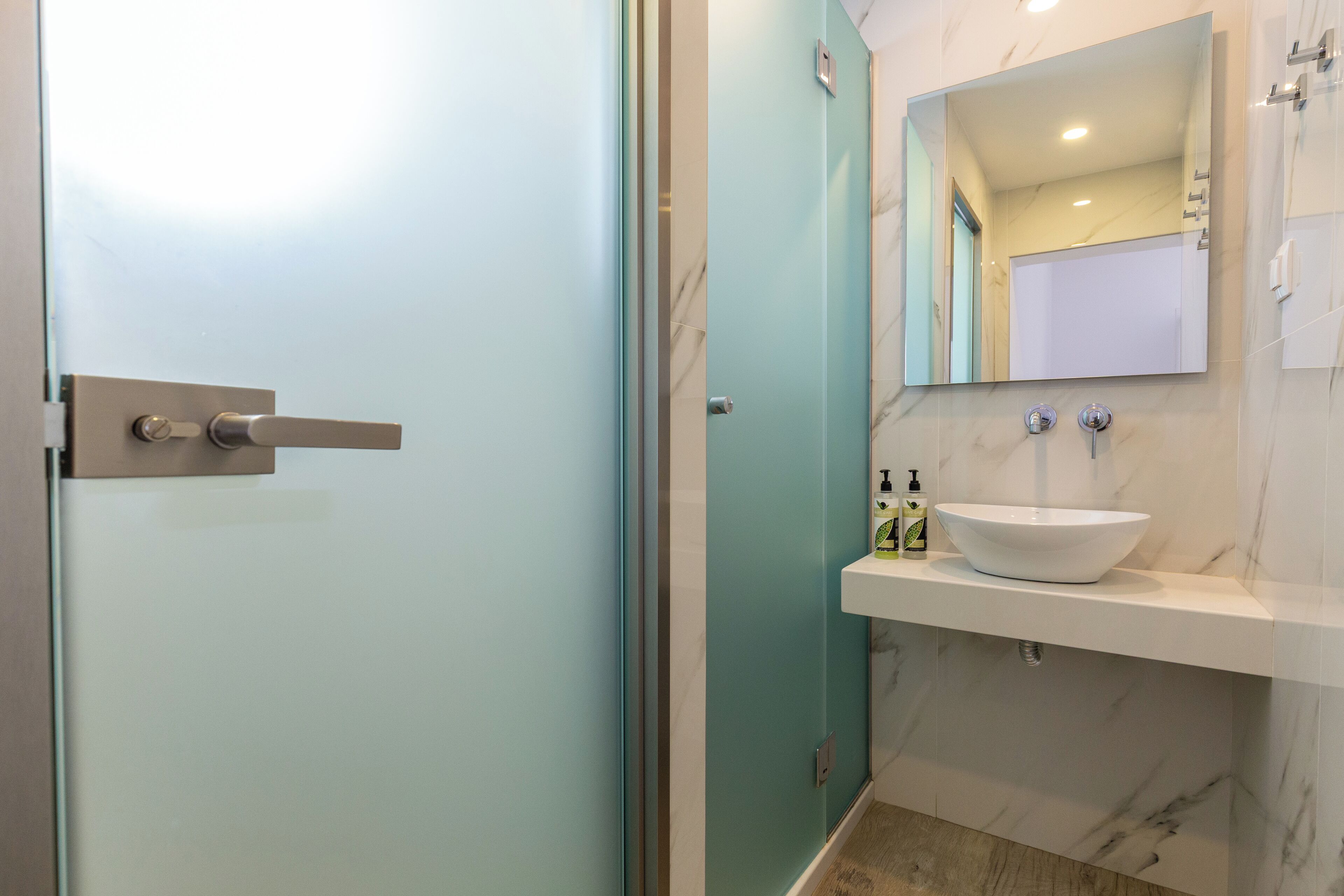 A modern bathroom with a glass door, a white sink, and a marble-tiled wall.