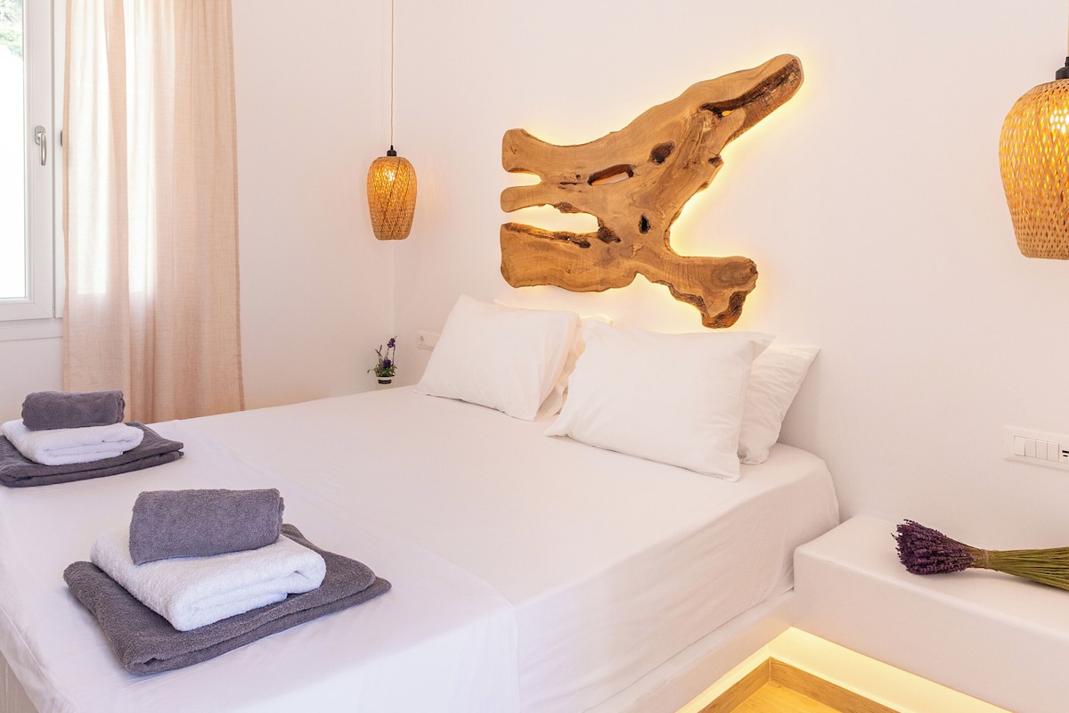 Une chambre à coucher moderne avec un grand lit, une tête de lit en bois et une table de chevet ornée d’un vase de fleurs.