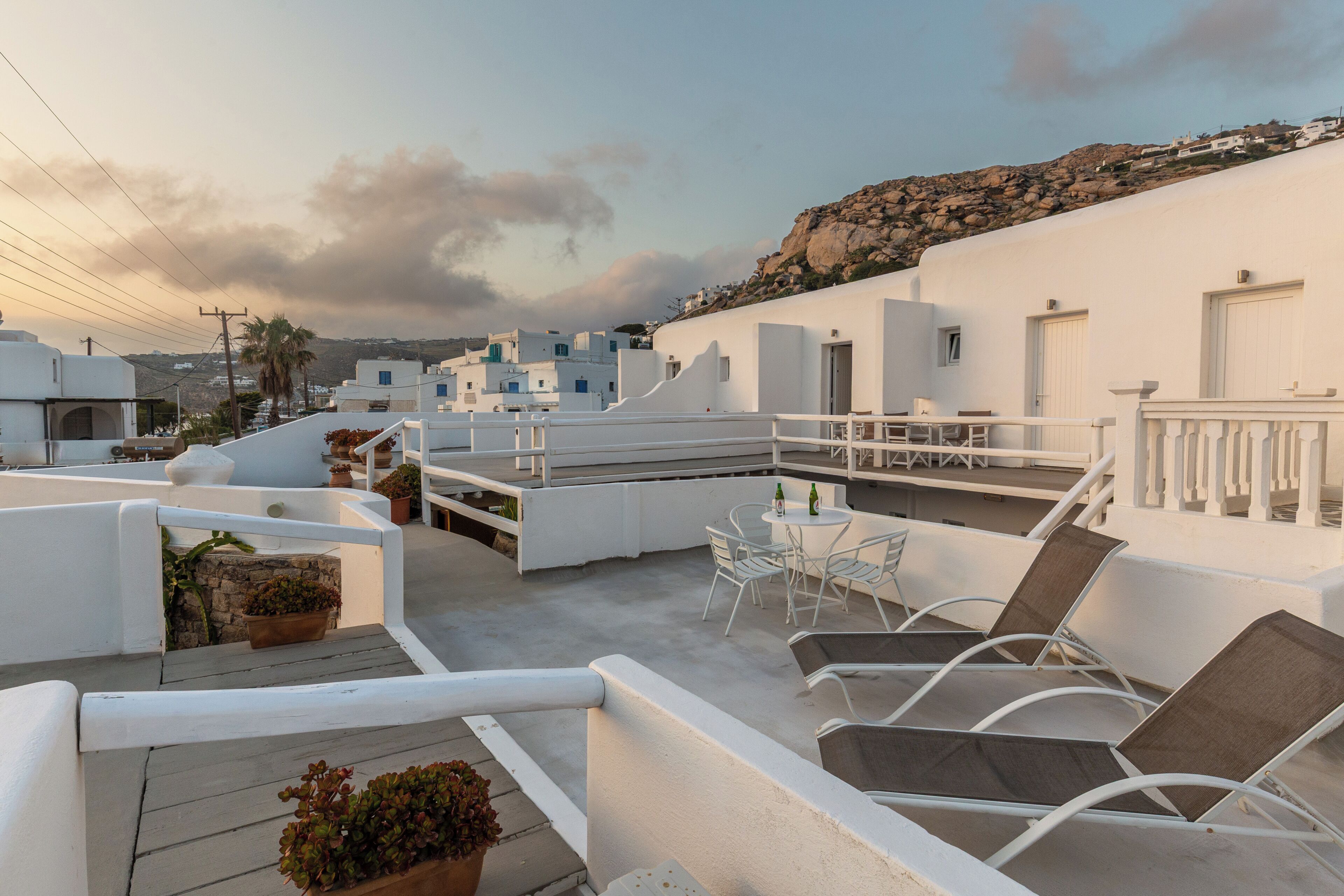 A rooftop terrace with white buildings, outdoor furniture, and a view of the landscape.