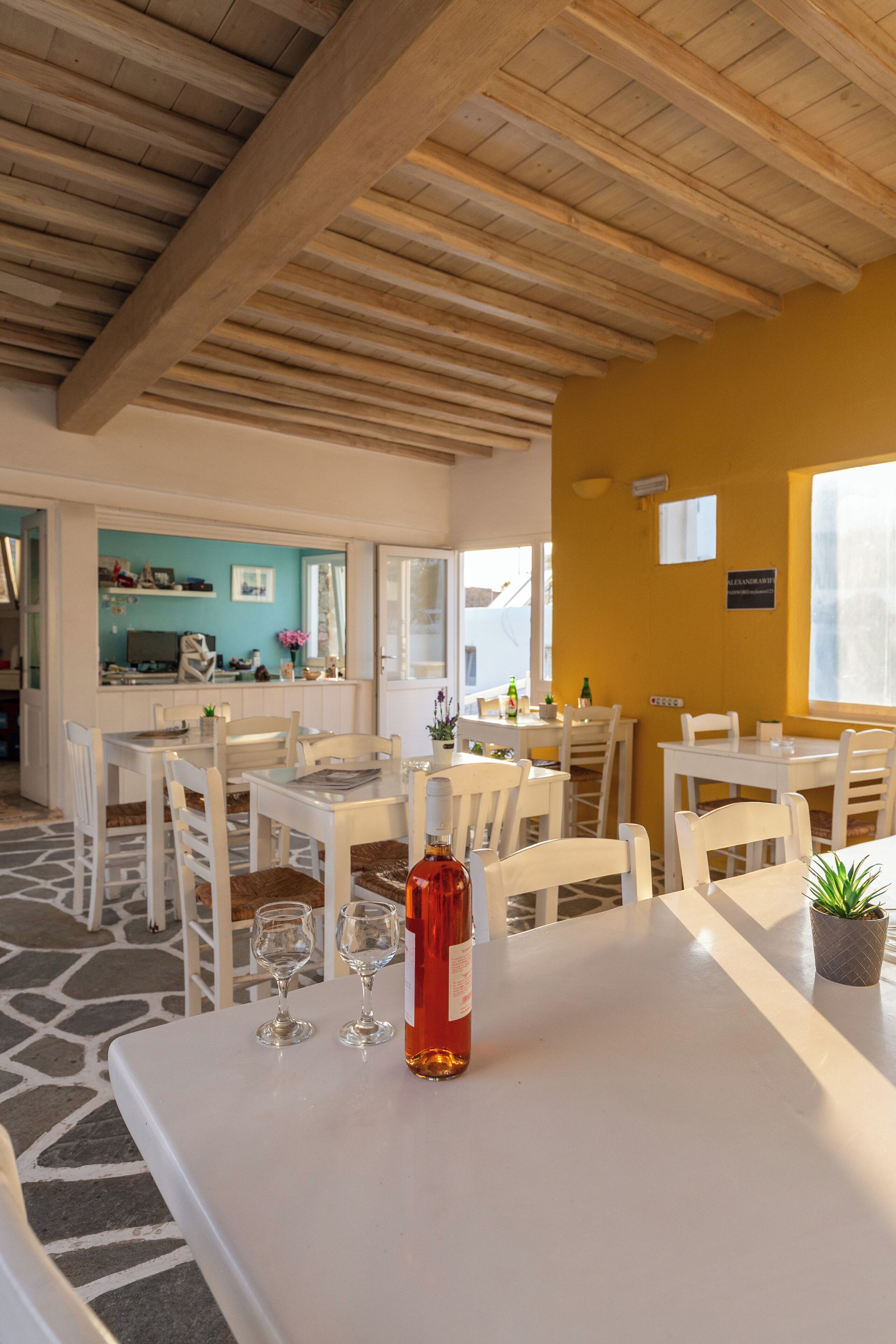 A dining area with white tables and chairs, a bottle of wine, and a small plant on the table.