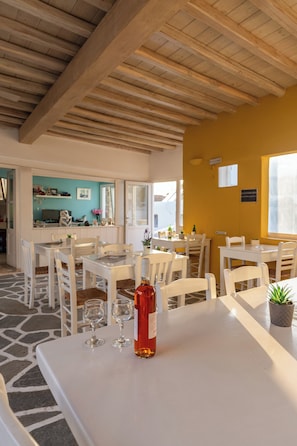 A dining area with white tables and chairs, a bottle of wine, and a small plant on the table.