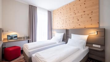 A hotel room with two beds, a desk with a laptop, a red ottoman, and a wooden accent wall.