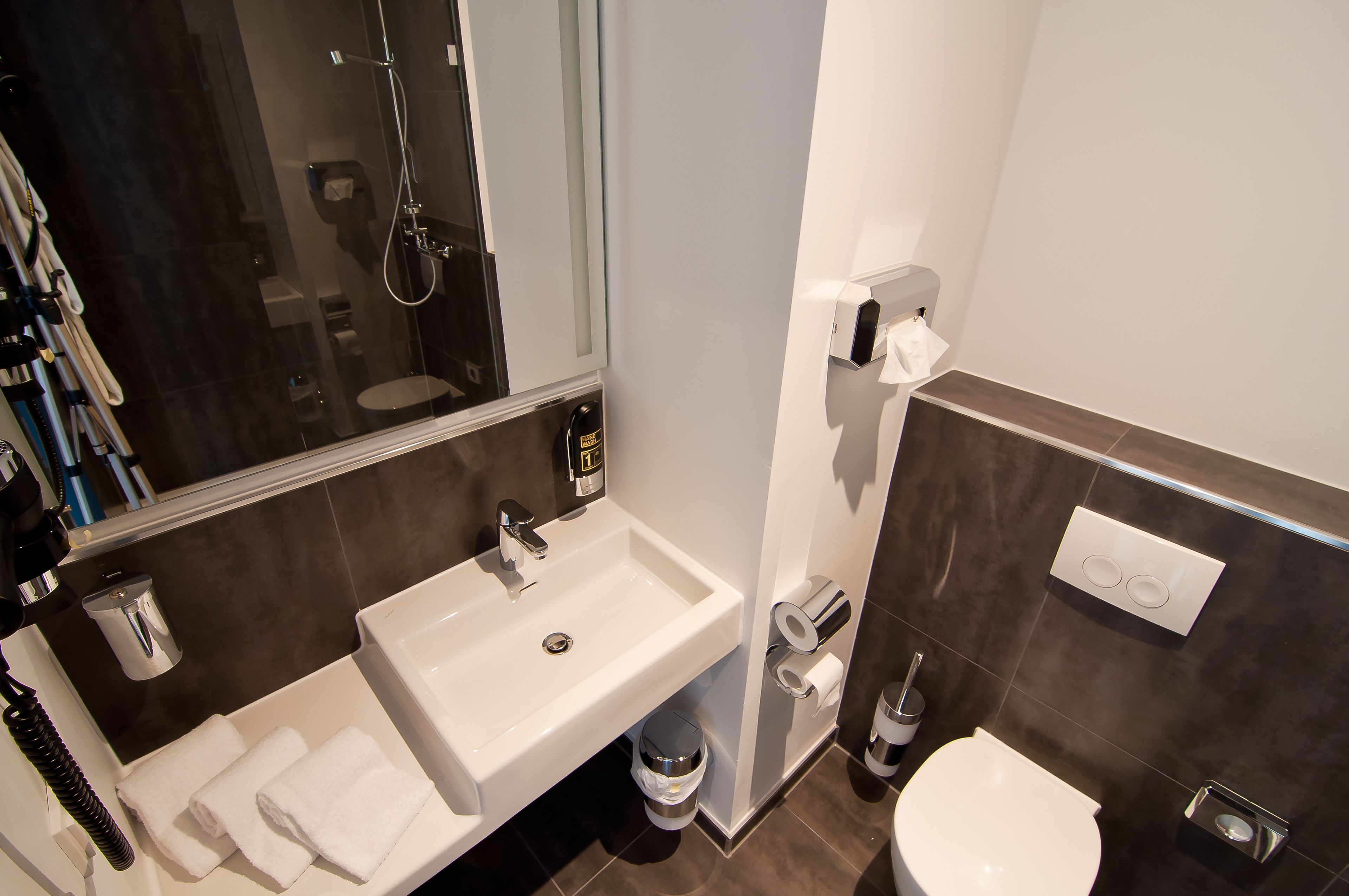Een moderne badkamer met een wit wastafel, spiegel en toilet. Er liggen handdoeken op de wastafel, een handdoekhouder en een toiletrolhouder.