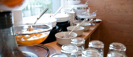 Een buffetopstelling met diverse kommen, lepels en toevoegingen op een houten tafel.