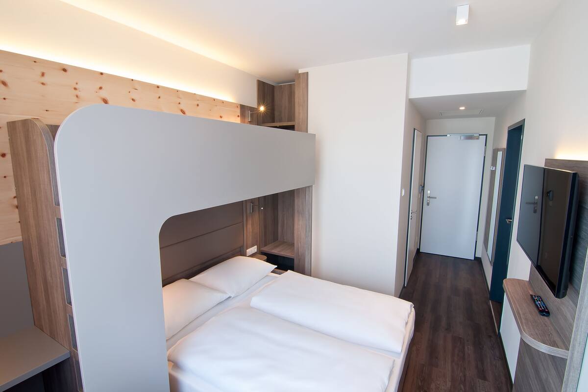 A modern hotel room with a bunk bed, a desk with a computer, and a television.