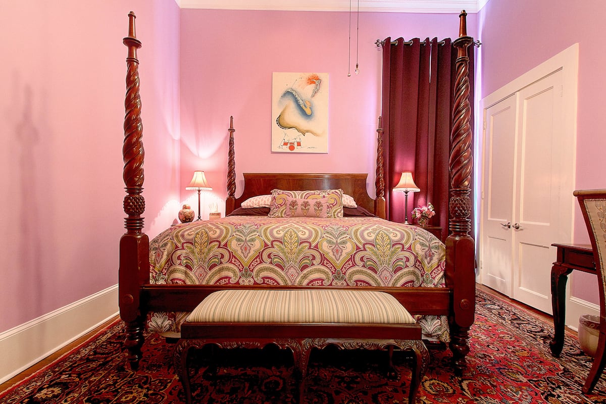 A four-poster bed with a patterned bedspread, a bench at the foot of the bed, and a painting on the wall.