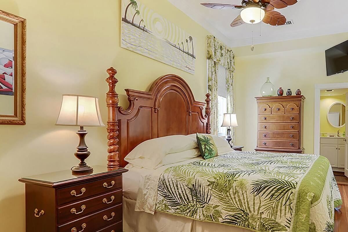 A bedroom with a wooden bed, a nightstand with a lamp, a dresser, and a ceiling fan.
