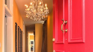 Um corredor com uma porta vermelha, um candelabro e um tapete estampado.