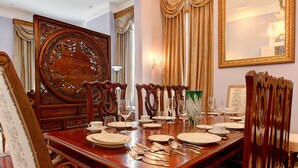 Uma sala de jantar formal com uma grande mesa de madeira posta para refeição, cercada por cadeiras ornamentadas e um espelho grande na parede.