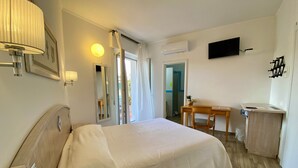 A hotel room with a bed, a desk, a chair, a TV, and an air conditioning unit. - Locanda degli Artisti (Tortoli)