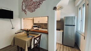 A modern kitchen with white cabinets, a stainless steel refrigerator, and a dining area with a table and chairs. - Locanda degli Artisti (Tortoli)