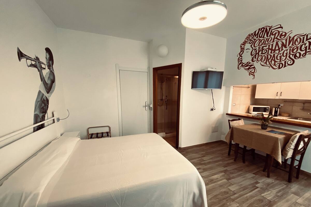A bedroom with a bed, a desk, and a shower.
