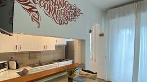 A modern kitchen with white cabinets, a wooden countertop, and a dining area with a table set for two. - Locanda degli Artisti (Tortoli)