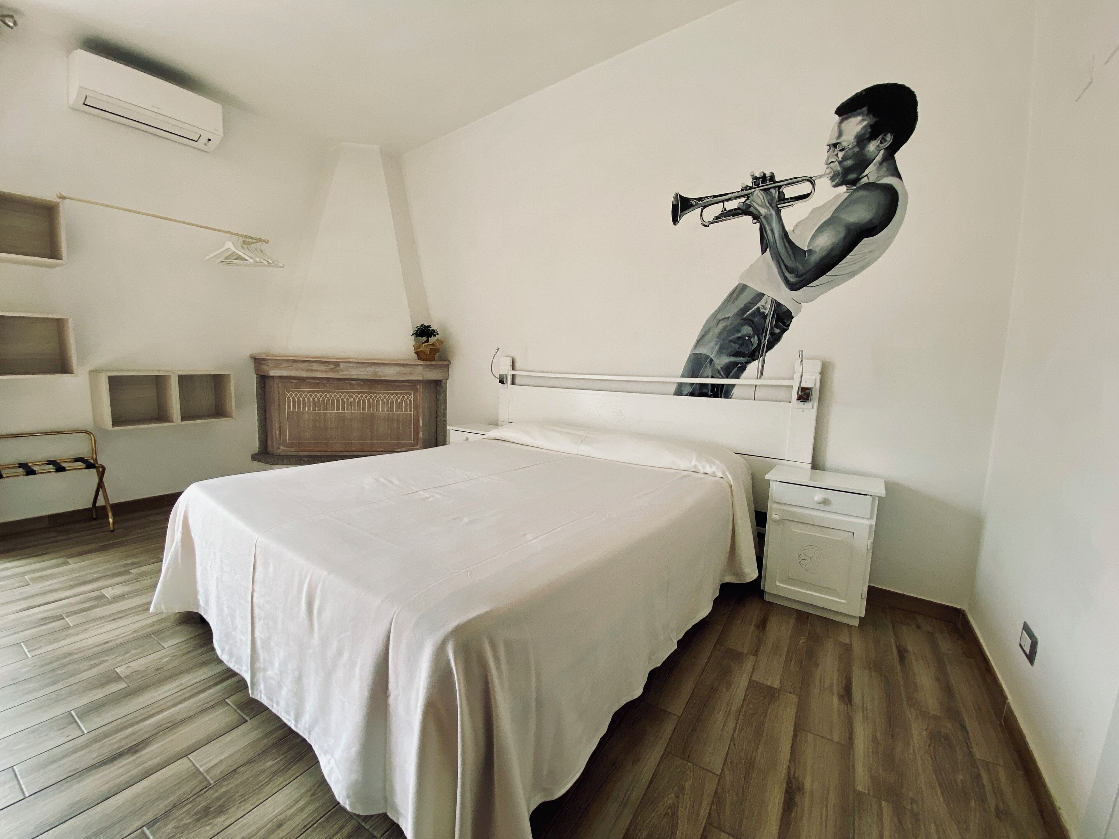 Un dormitorio con cama, mesita de noche, cómoda, planta colgante y aire acondicionado instalado en la pared.