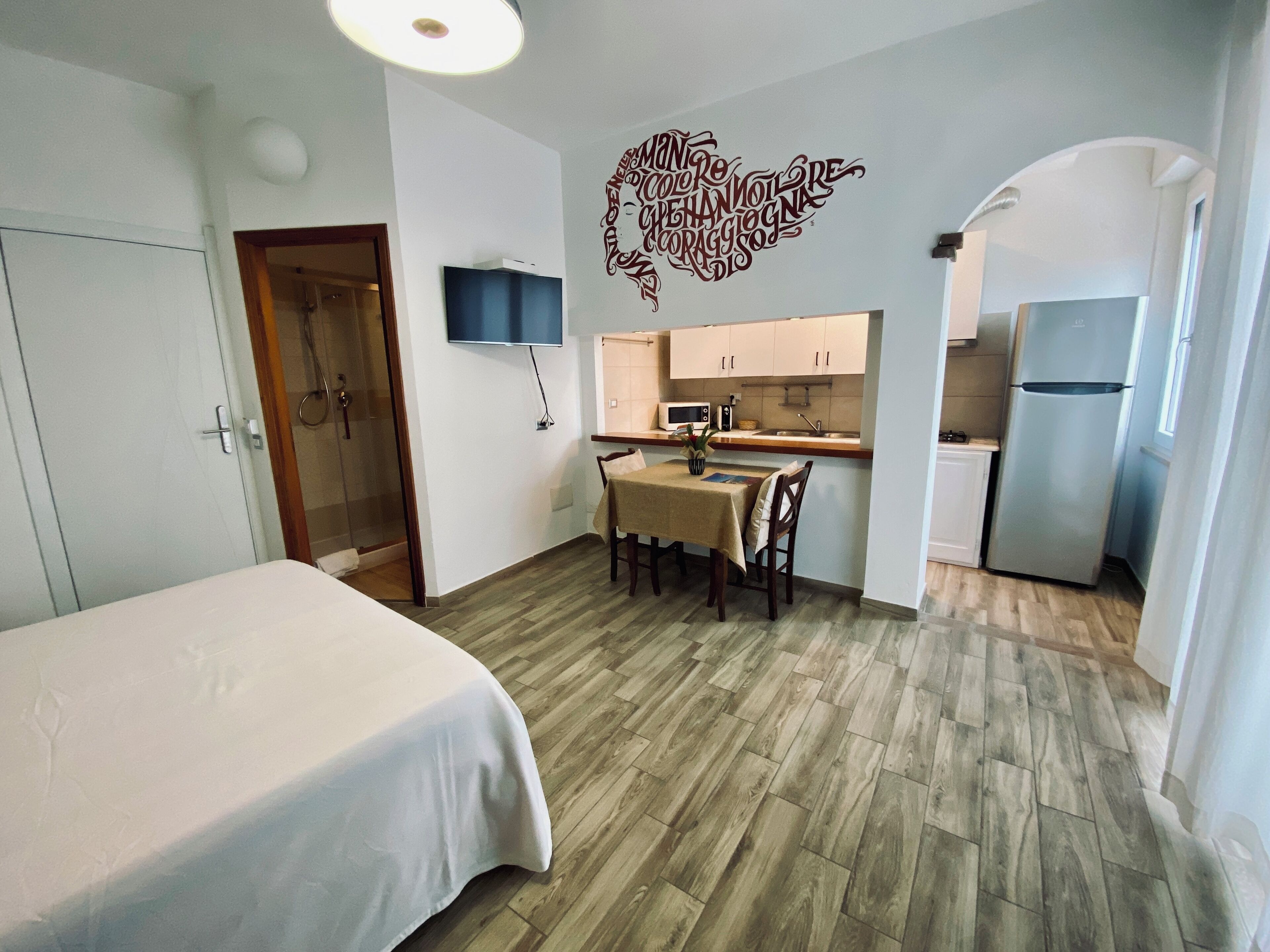 Una habitación de hotel compacta con cama, mesa de comedor, kitchenette y ducha.