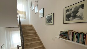 A staircase with a handrail, a wall-mounted shelf with books, and framed pictures. - Locanda degli Artisti (Tortoli)