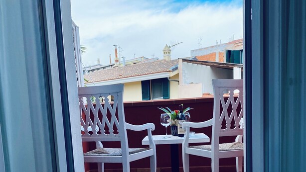 A balcony with two white chairs and a small table, overlooking a residential area with buildings and a clear sky. - Locanda degli Artisti (Tortoli)