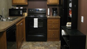 A kitchen with wooden cabinets, a black stove, a microwave, a coffee maker, and a refrigerator. - Eagle Ford Lodging (Pleasanton)