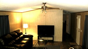 A living room with a leather sofa, a television, a coffee table, and a ceiling fan. - Eagle Ford Lodging (Pleasanton)