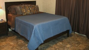 A bedroom with a bed, a nightstand, a lamp, and a curtain. - Eagle Ford Lodging (Pleasanton)