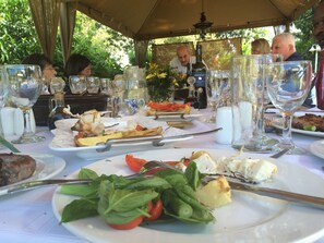 An outdoor dining area with tables set for meals, featuring plates of food, wine glasses, and cutlery.