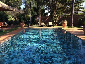 Una piscina rectangular con mosaicos, rodeada por un muro de ladrillo y plantas en macetas.